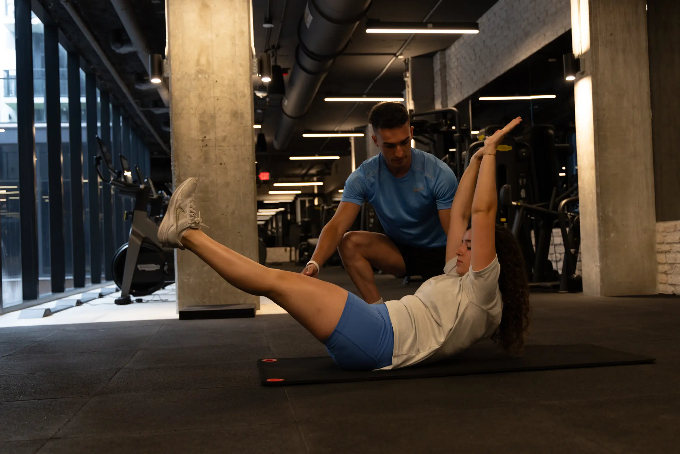 Trainer assisting a client with a supported core exercise on a mat